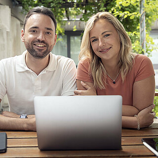 Ein Mann und eine Frau sitzen in einem Innenhof vor einem Laptop