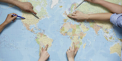 Hände zeigen auf Weltkarte